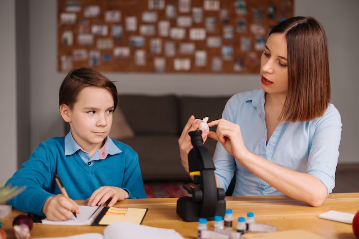 A woman and a child engage in a science activity, examining specimens with a microscope on a wooden table filled with lab materials.