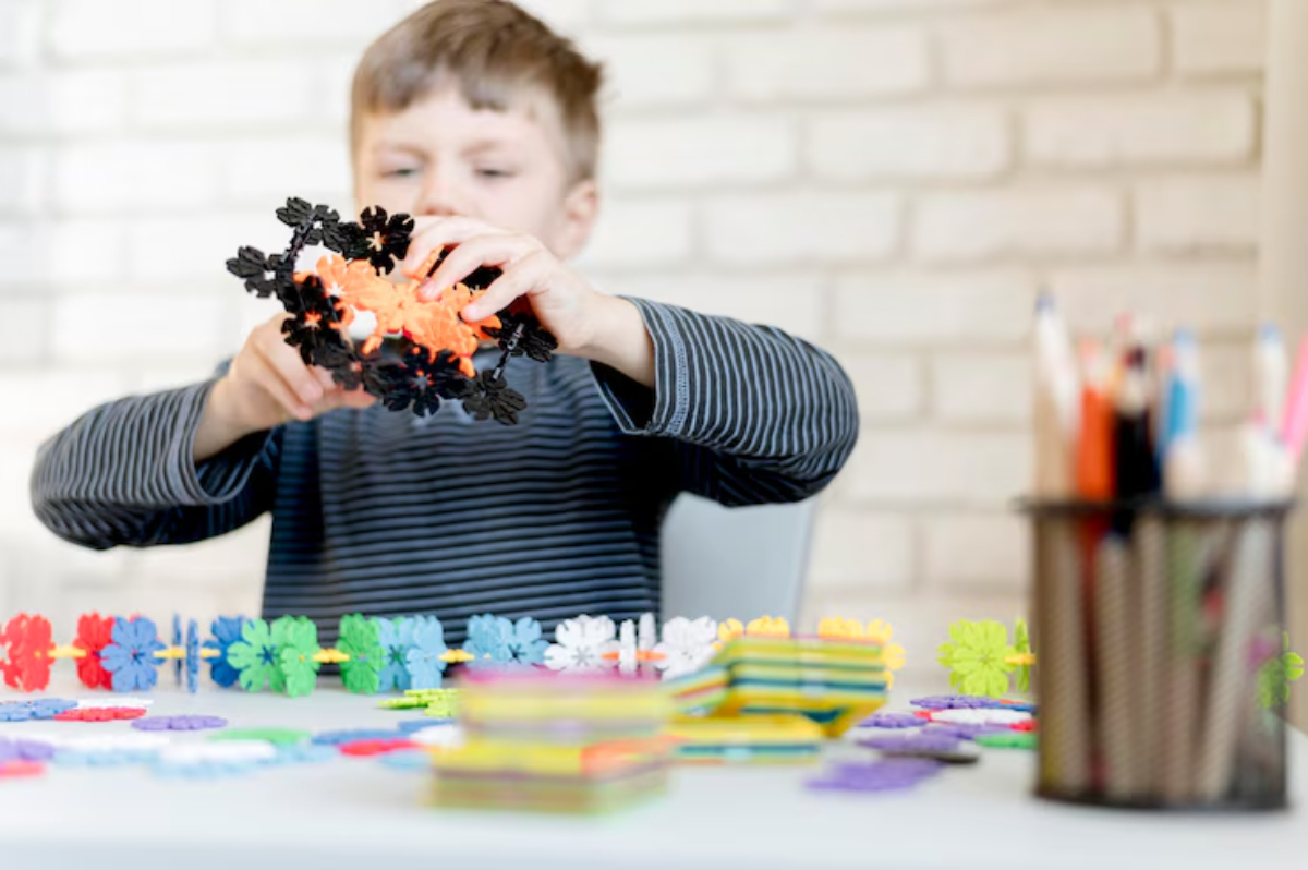 A child in a striped shirt is holding a colorful construction toy amidst various vibrant pieces on a table, showcasing creativity.