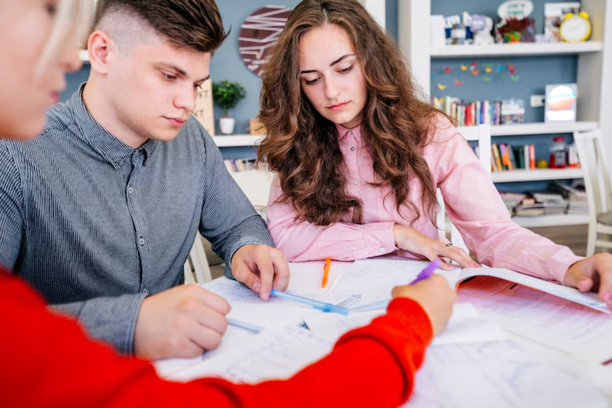 Three individuals collaborate at a table scattered with papers and stationery, engaging in a thoughtful discussion.