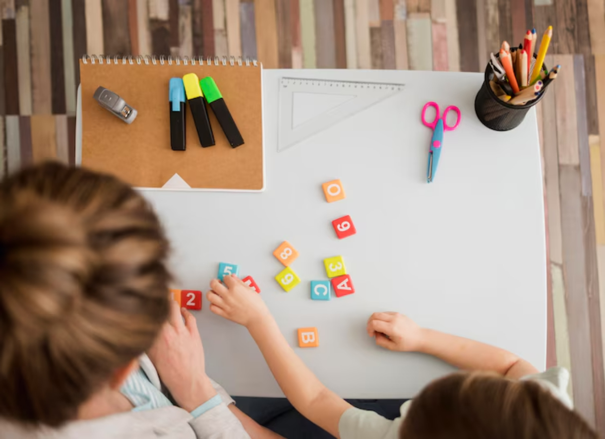 A child and adult arrange colorful number blocks on a desk, surrounded by stationery like markers, scissors, and a notebook.