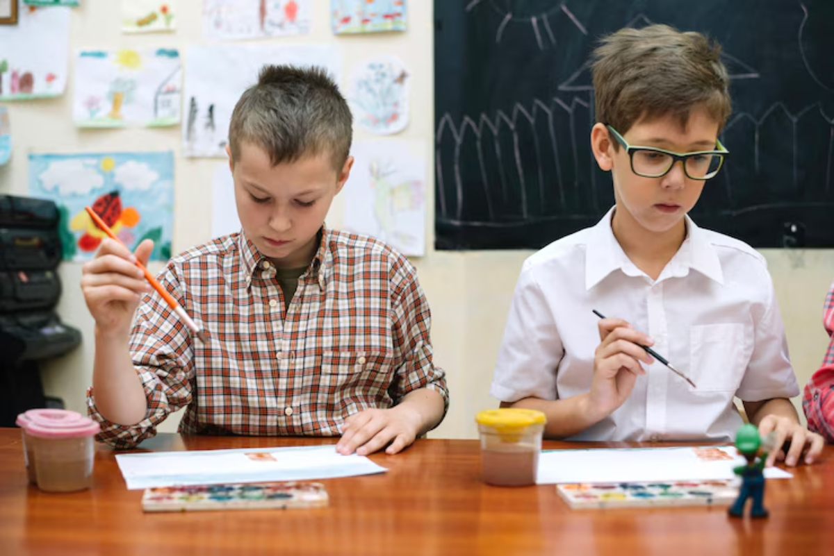 Two children sitting at a table, engaged in painting, surrounded by colorful artwork on the walls and art supplies on the desk.