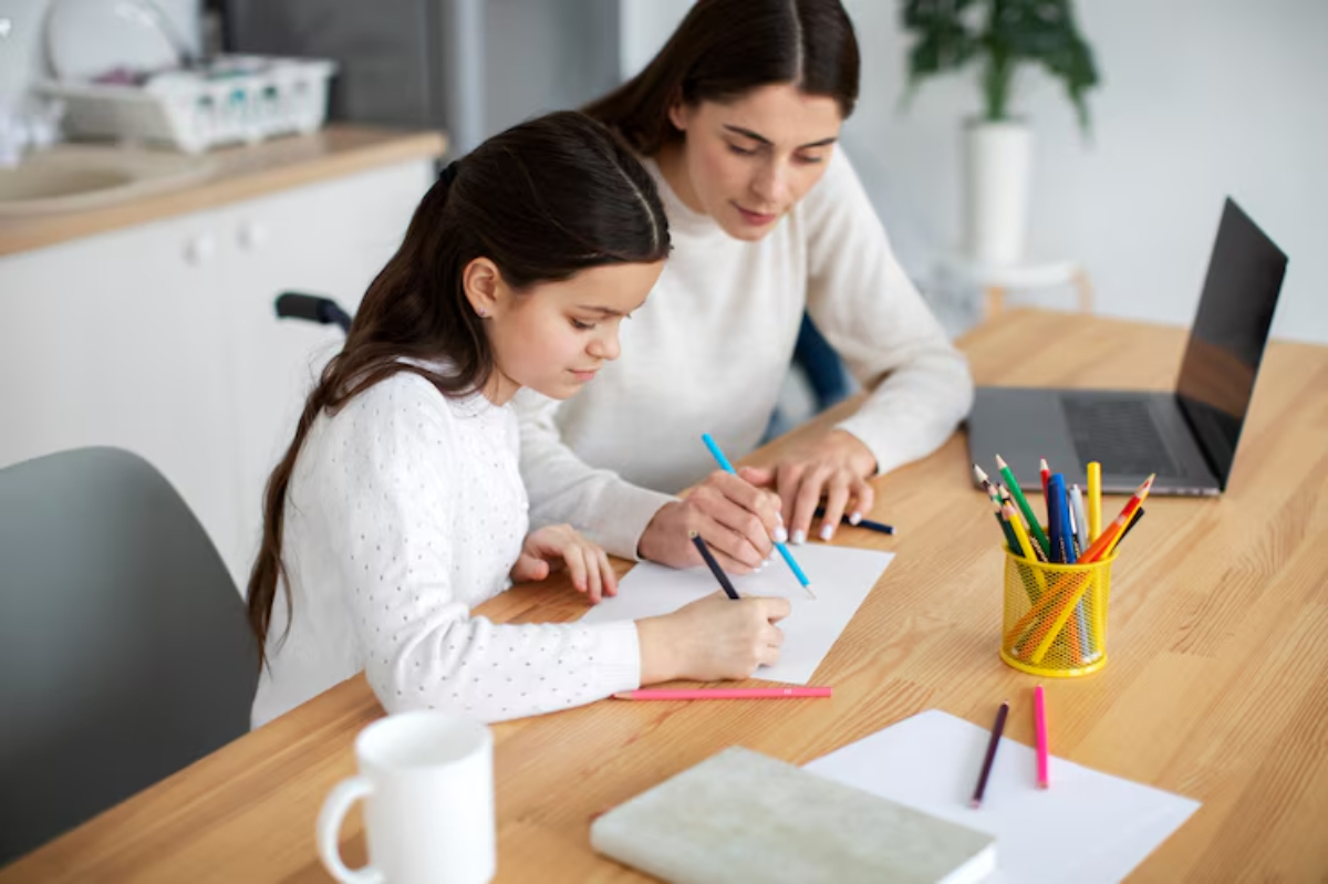 A child and adult engage in a creative activity, drawing with colored pencils at a wooden table, surrounded by art supplies and a laptop.