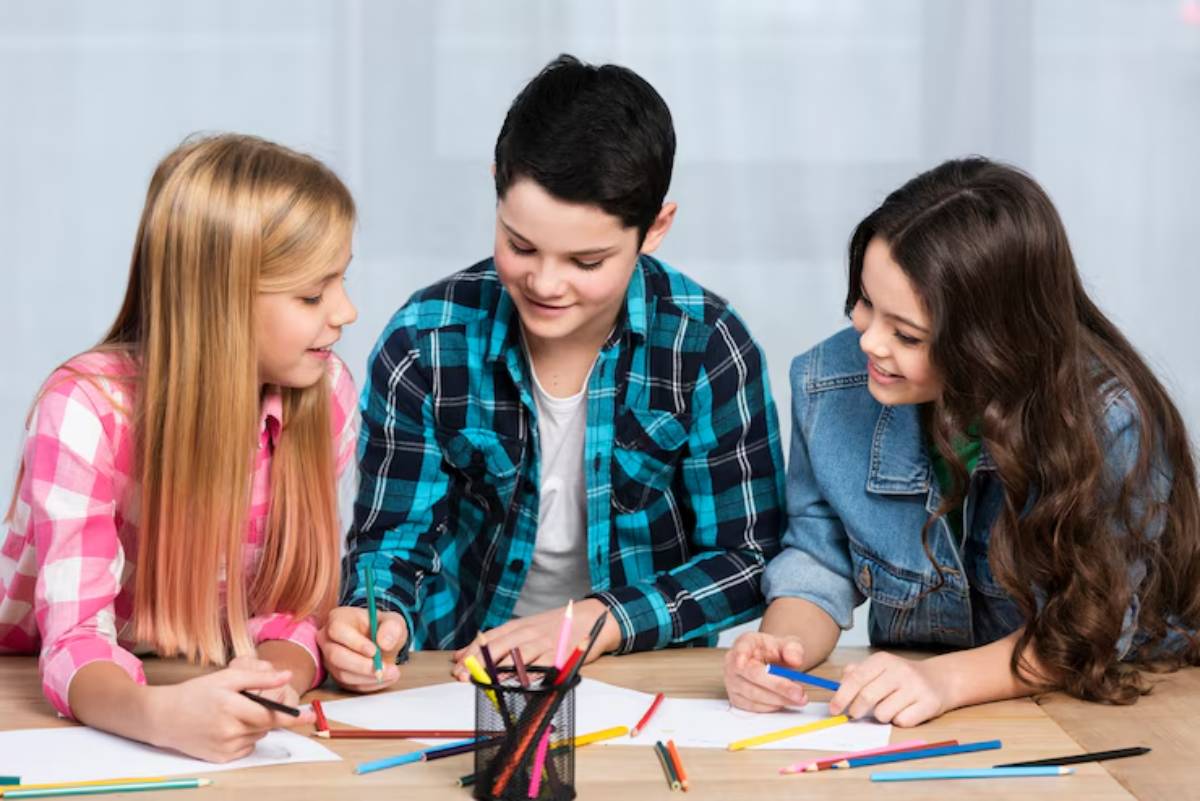 Three children engaged in creative drawing, surrounded by colorful pencils on a wooden table with papers in front of them.