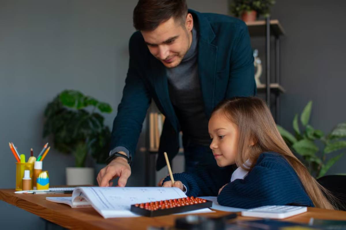 A person assists a child with homework at a wooden desk, surrounded by stationery, books, and greenery in a cozy room.