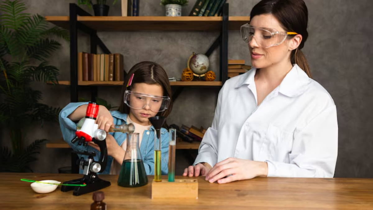 A young girl uses a microscope while conducting an experiment, assisted by a woman in a lab coat, with colorful liquids on the table.