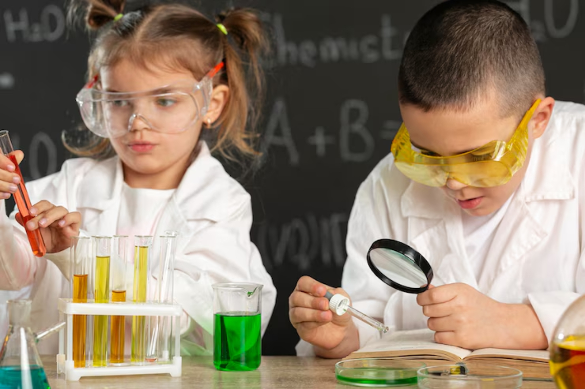 Two children in lab coats conduct experiments with colorful liquids in test tubes and beakers, surrounded by a chalkboard backdrop.