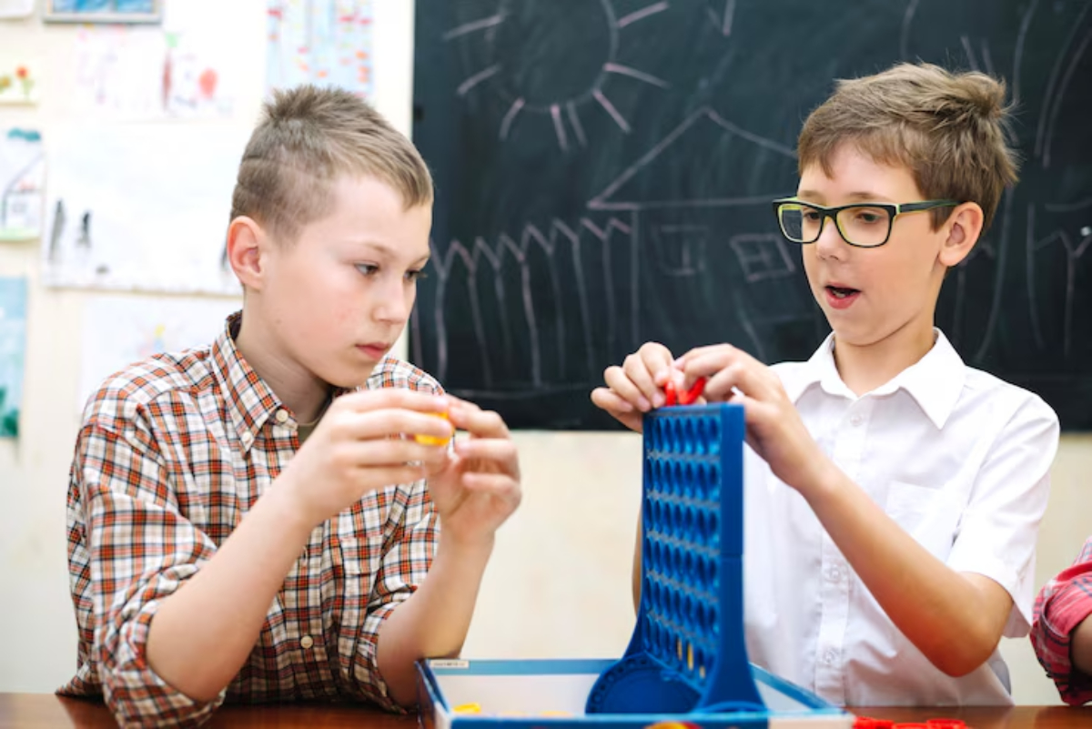 Two children play a board game at a table, focusing on connecting colored pieces in a game of strategy, with artwork in the background.