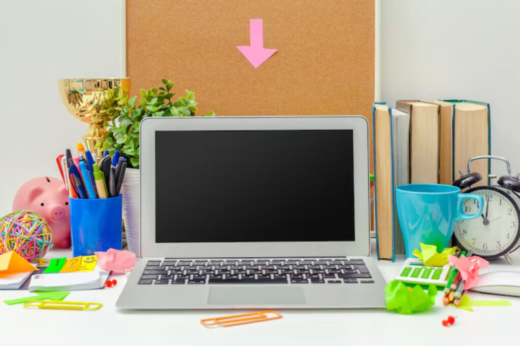 A cluttered desk with a laptop, books, plants, office supplies, a clock, and a piggy bank, creating a vibrant workspace atmosphere.
