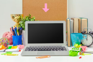 A cluttered desk with a laptop, books, plants, office supplies, a clock, and a piggy bank, creating a vibrant workspace atmosphere.