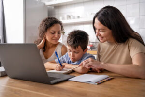 Three individuals engage in a collaborative learning activity at a wooden table, with a laptop and notebooks in front of them.