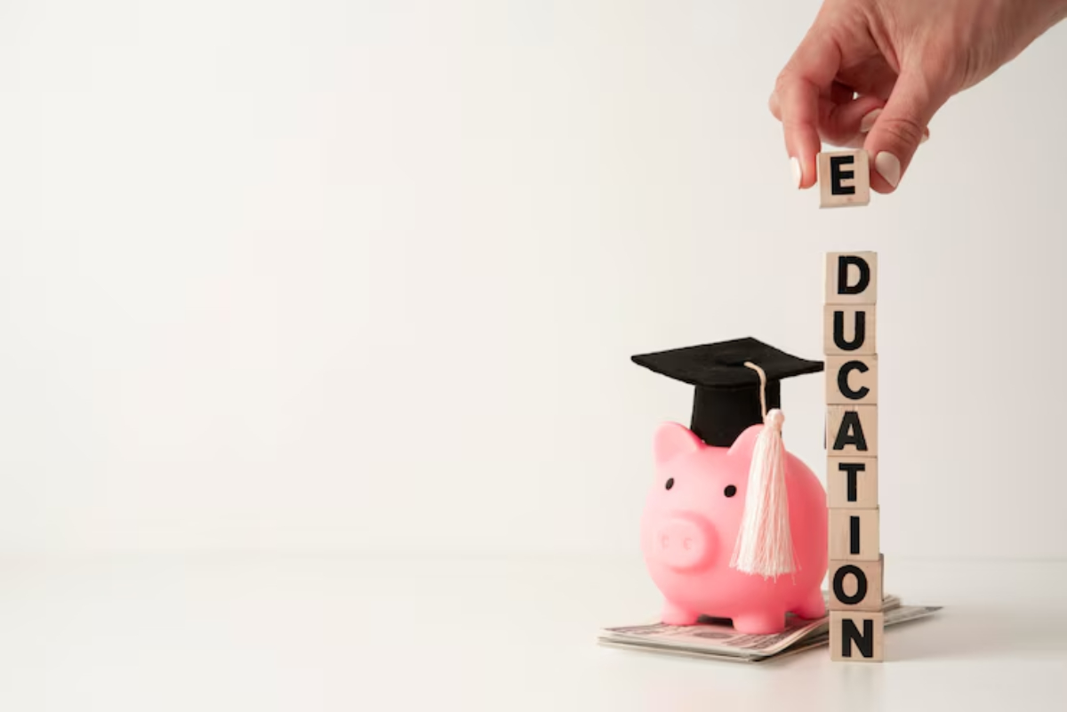 A hand places a block labeled E atop a stack spelling EDUCATION next to a piggy bank with a graduation cap, symbolizing education savings.